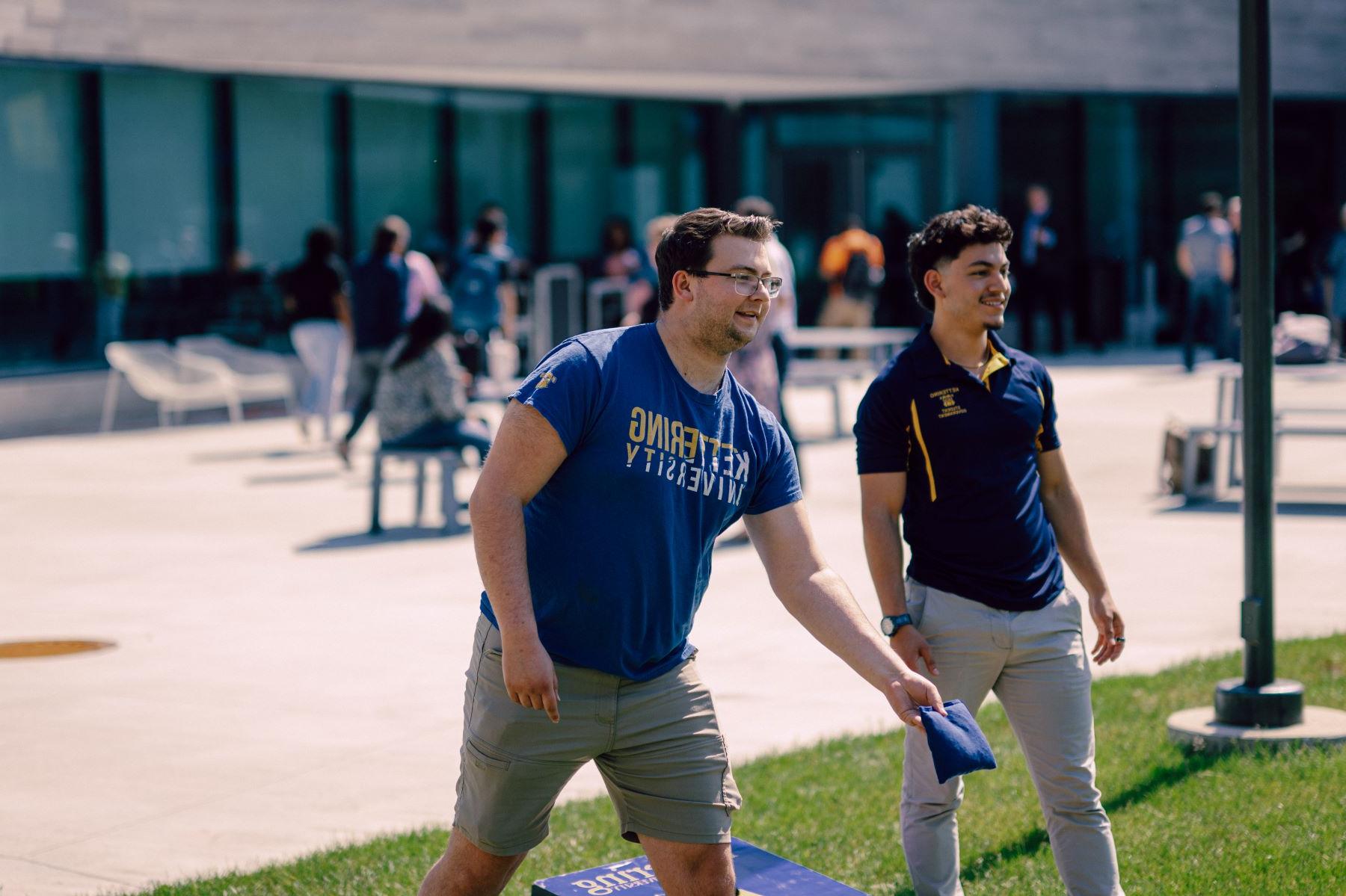 Two Kettering students play cornhole by the Learning Commons. One student holds a bean bag and readies his throw.